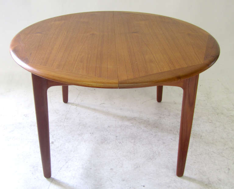 This circular Danish dining table features a classic modern frame and beautifully displays the natural grains of the teak on the surface. There are two extensions found underneath the table, as pictured. They unfold when you open the table. Marked