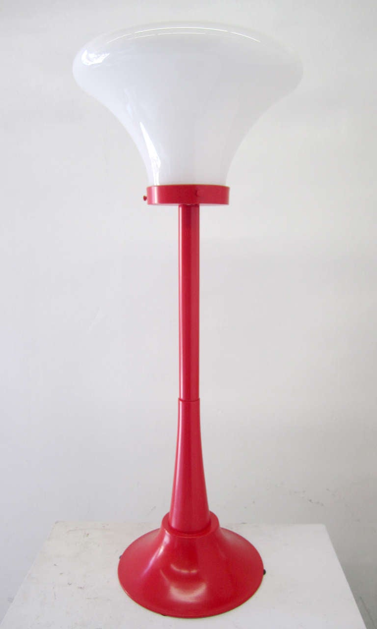 This mid-sized lamp, which can be displayed on either the table or the floor, is comprised of a strong base and a large, bell-shaped exposed lightbulb. The metal base has recently been repainted cadmium red.