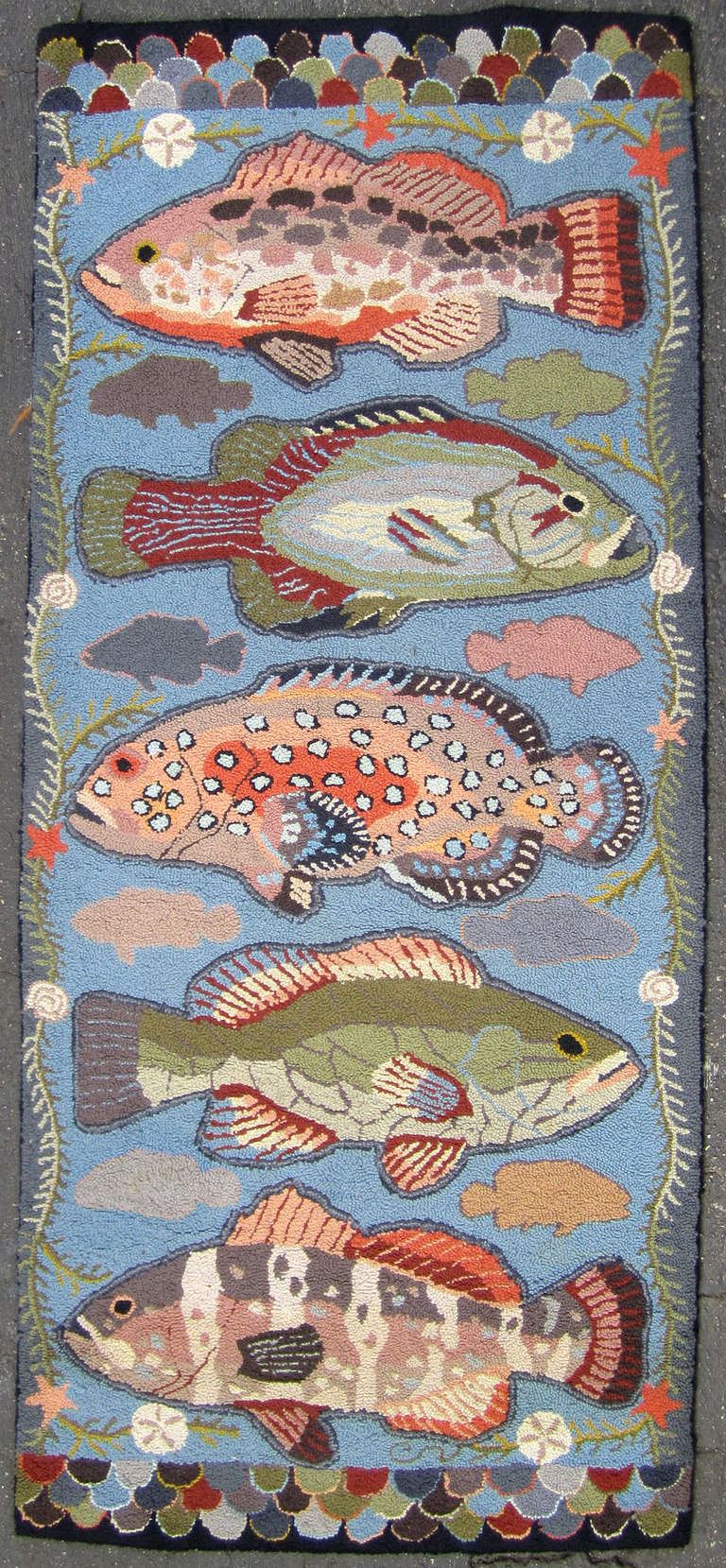 This unusual hooked rug employs great detail and whimsy in its depiction of  five large fish framed by a starfish garland and finished on each end with colorful scales.