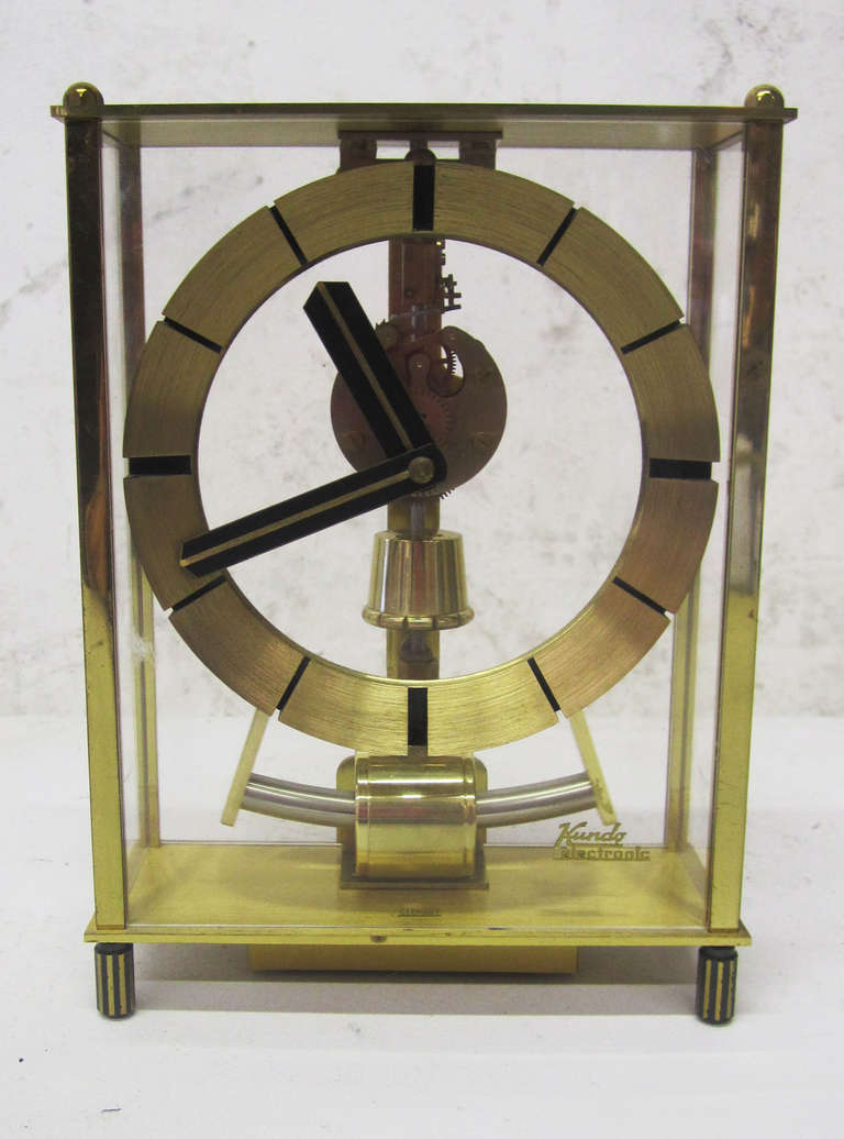 This mid-century modern clock by the German company Kundo features a minimal brass frame and face encased in glass. The skeleton clock is operated by a single AA battery.