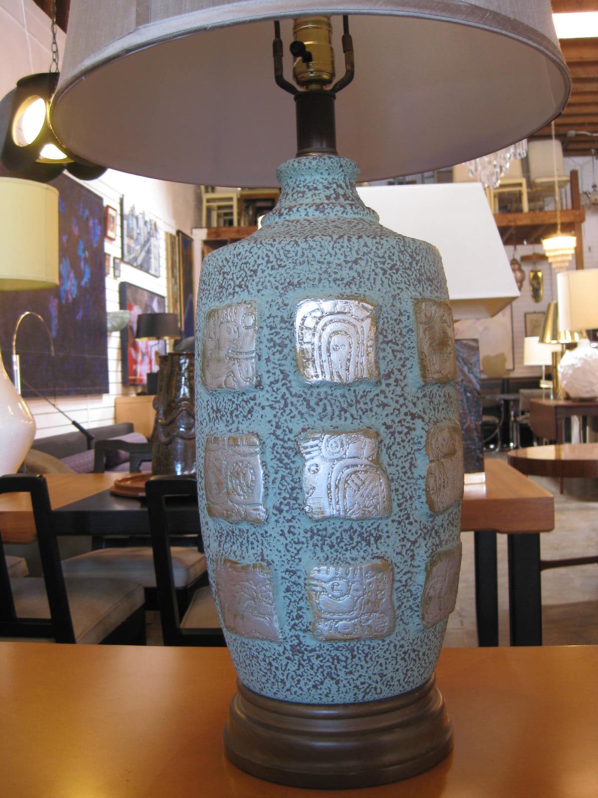 Handsome pair of light teal ceramic table lamps with wood base. Eighteen silver-plated Mayan hieroglyphs, 9 per each side, decorate the frontal of each piece. The base is made of solid wood. Included, as shown with each lamp is a 16