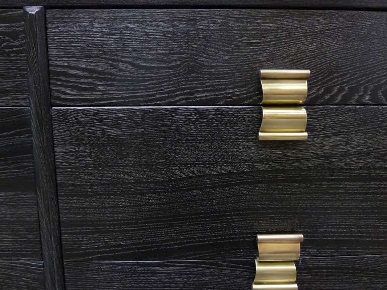 The oak of this Paul Frankl dresser has been  ebonized with white ceruse in the grain. It features 6 comfortable drawers with brass undulating pulls.
