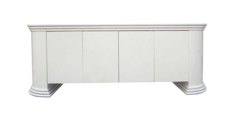 This handsome credenza from the 1980s features a pearl-toned lacquer finish. Four push-to-to-open doors reveal shelving on both sides with a narrow drawer on the right. The ovular frame terminates in two minimal columns which gives the piece a