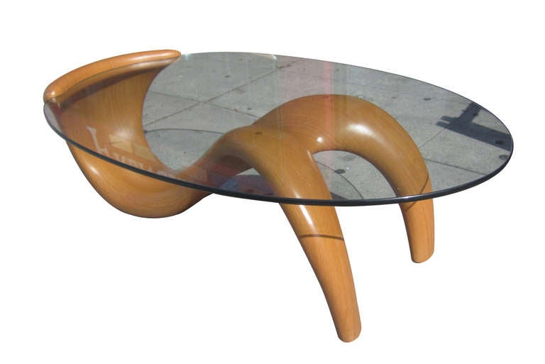 This biomorphic coffee table from the 1980s features an undulating maple finish fiberglass base which hugs the glass surface on one end while supporting it from beneath towards the other end.
