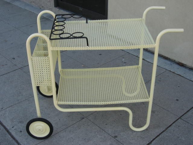 A smoothly rolling two level tea cart by Mathieu Mategot in yellow painted finish with single bent steel tube construction detailed with eight glass holders and four slotted bays for bottles.