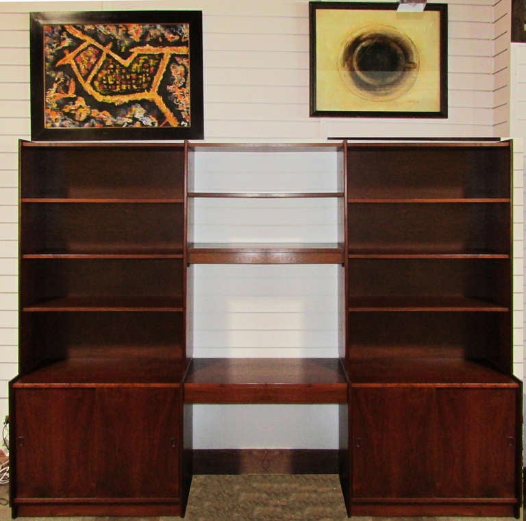This Danish modern wall unit features a pair of cabinets surmounted by bookshelves flanking a central bay with a writing desk complete with a hidden light and open shelving above. The unit is made of walnut.