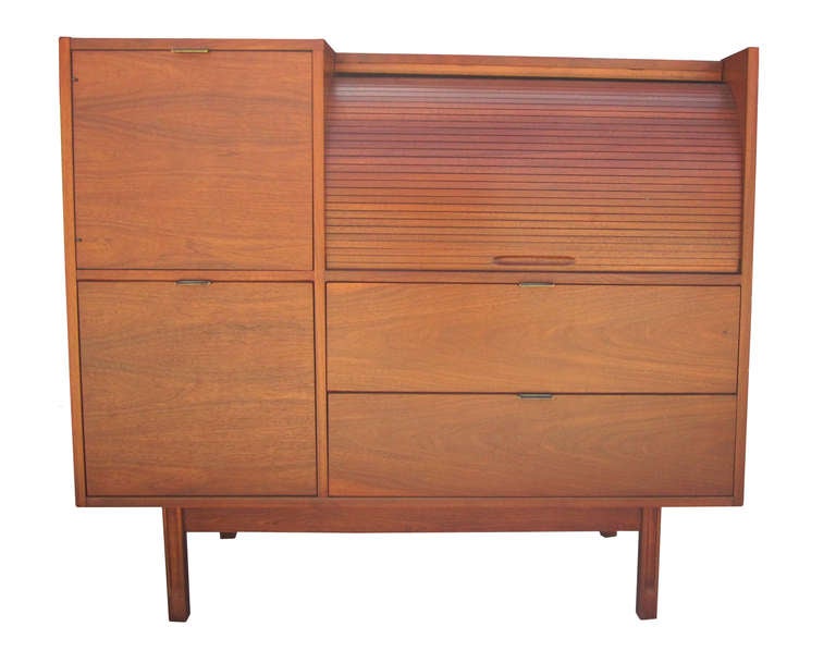 This exquisitely designed, mid-century desk offers a myriad of storage options including a file drawer plus five other drawers and multiple open bays. There is a pull-out writing surface concealed behind a tambour door. The walnut desk is  ideal for