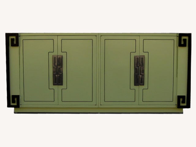 The body of this credenza is light green lacquer and has four brass-welted doors accented by heavy solid brass pulls and backing plates. The four front doors open and reveal top drawers and open shelving. All outer corners are adorned with heavy