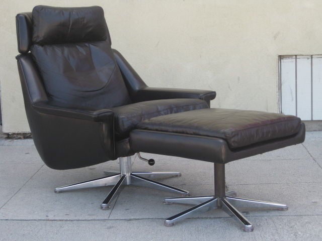 Low profile lounge armchair and ottoman  from the 1960's. The chair is upholstered in black leather with a chrome plated steel swivel base. The base has a lever at the base of the seat that can be pulled to adjust the seat height. Low armrests and a