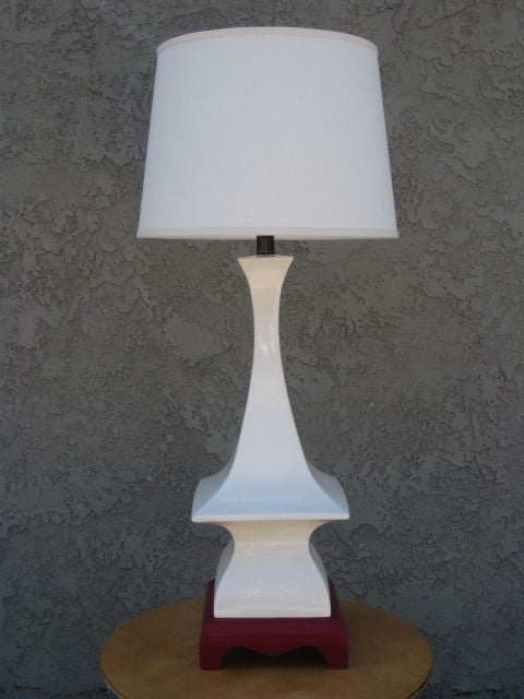 Table lamp in white ceramic glaze from the 1960's. The flared body of the lamp rests on a deep red wood base and has a distinctive Japanese architecture silhouette.