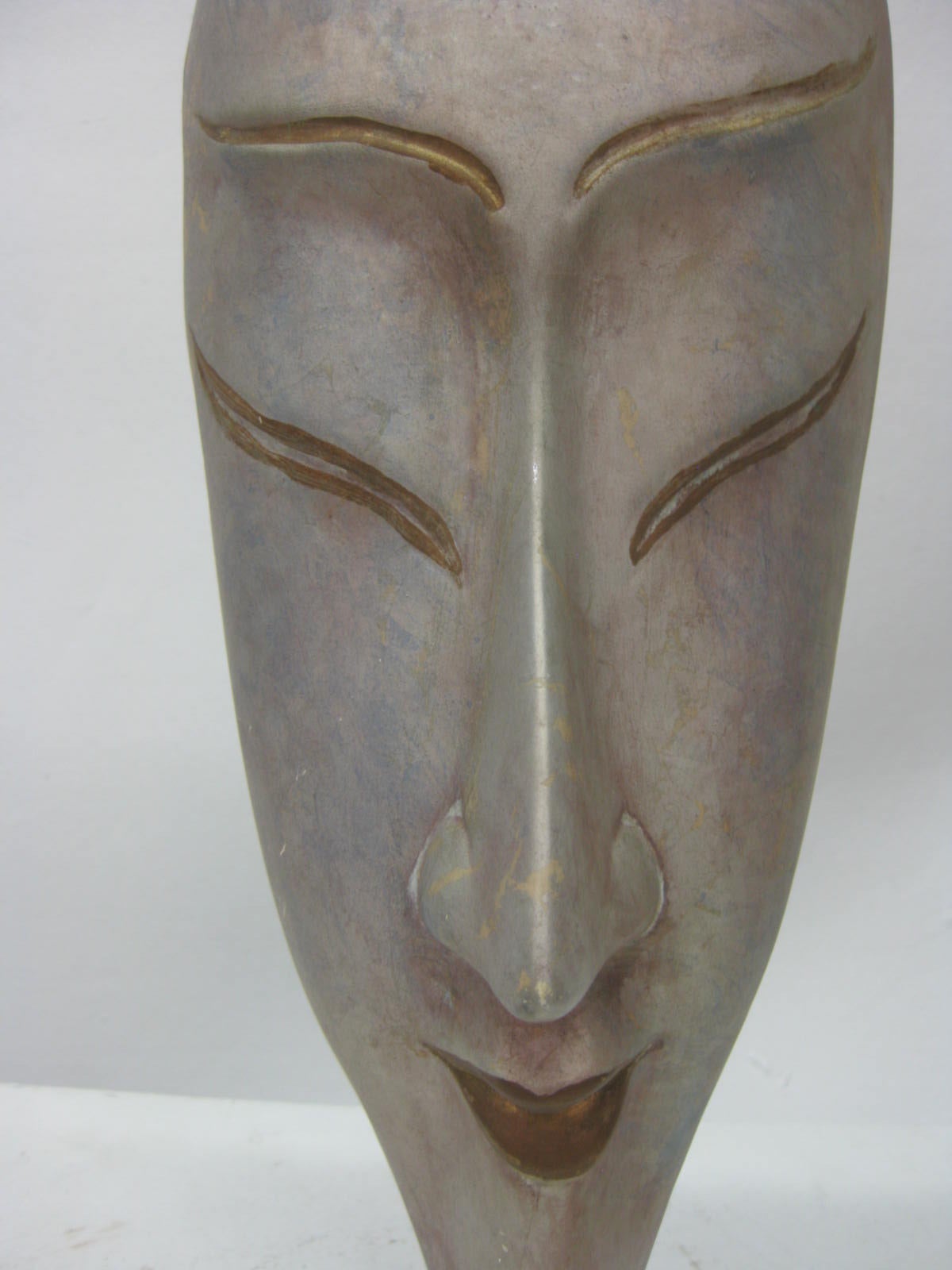 This hand-painted mask featuring a female face. Gold accents that highlight lips and eyes suggest Japanese culture.
It is resting on a clear Lucite mounted base.
