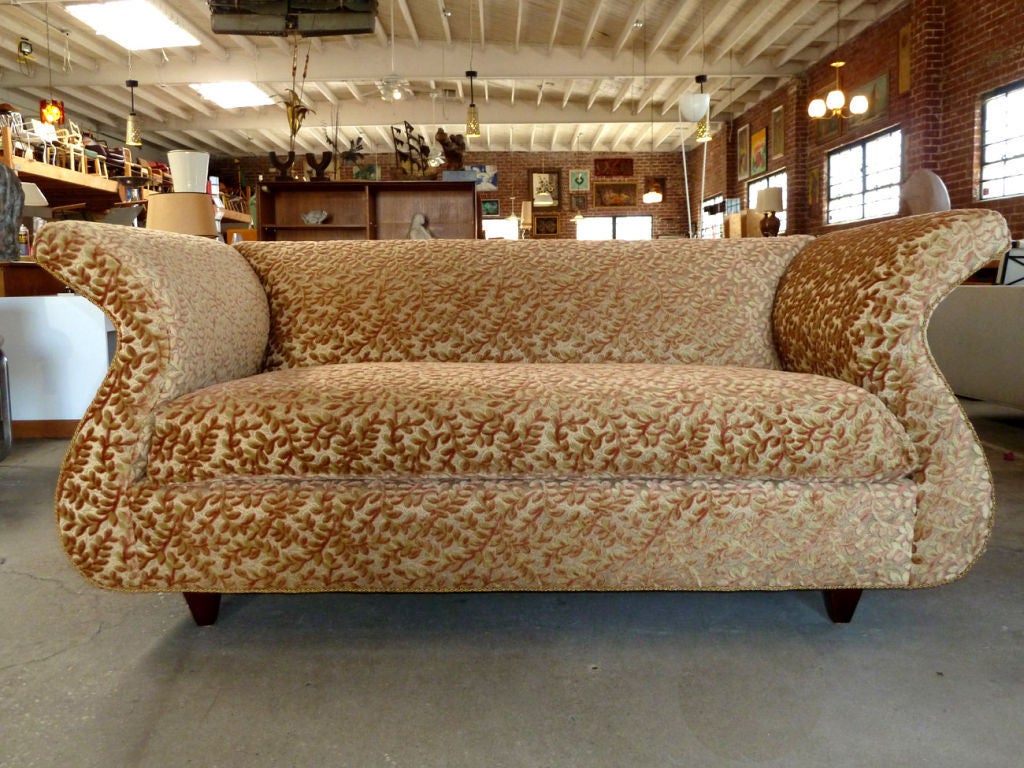 Upholstered love seat sofa designed by Dialogica from the 1980's. The sofa is upholstered in an intricate floral pattern using warm color tones. The sofa armrests and backrest distinctly curve out with a subtle flare giving the design a playful yet