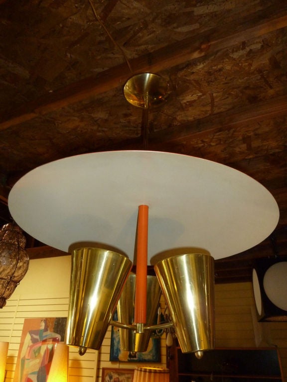 The saucer lamp has three perforated brass and inverted cone that shoot light up to a reflective saucer shade which bounces the light down and peripherally. The top of the shade and the shaft are painted in a light orange.