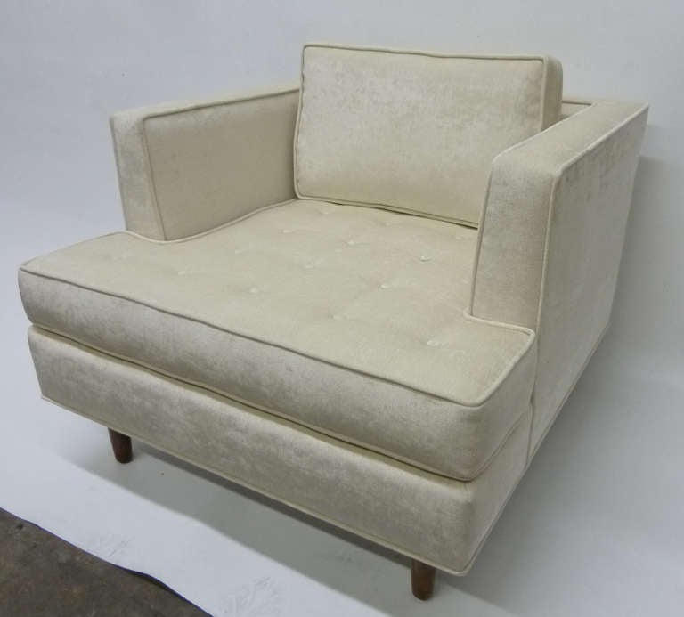 This Mid-Century Modern style pair of club chairs feature square frames, a loose back cushion and a tufted seat. They are upholstered in cream chenille and rest in slightly tapered walnut legs. These are a modern reinterpretation of Harvey Probber