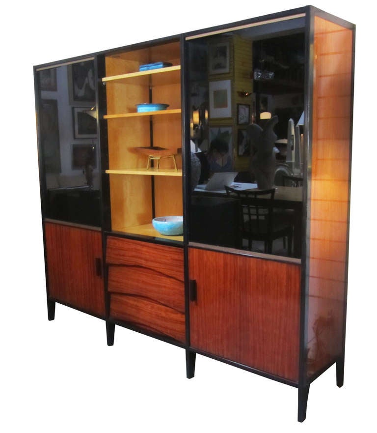 This midcentury French bookshelf features a glossy, mahogany frame, an open central display flanked by black glass sliding doors, and two lower cabinets with a set of drawers.