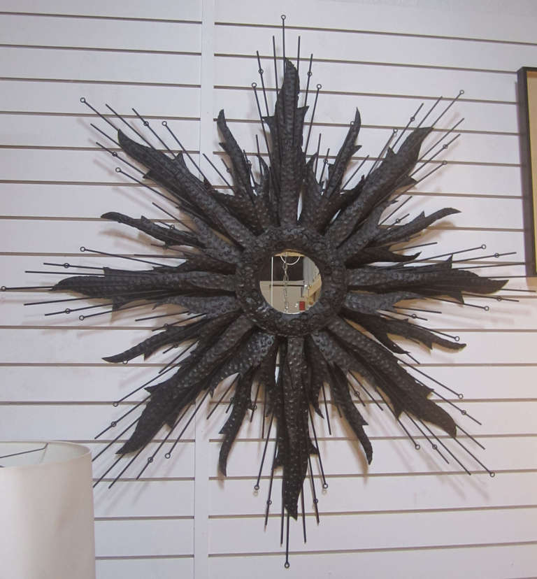 This circular wall-hanging mirror features a Brutalist frame in textured strips of metal mixed with iron rods of varying lengths. The mirror face itself is petite, measuring at just 7