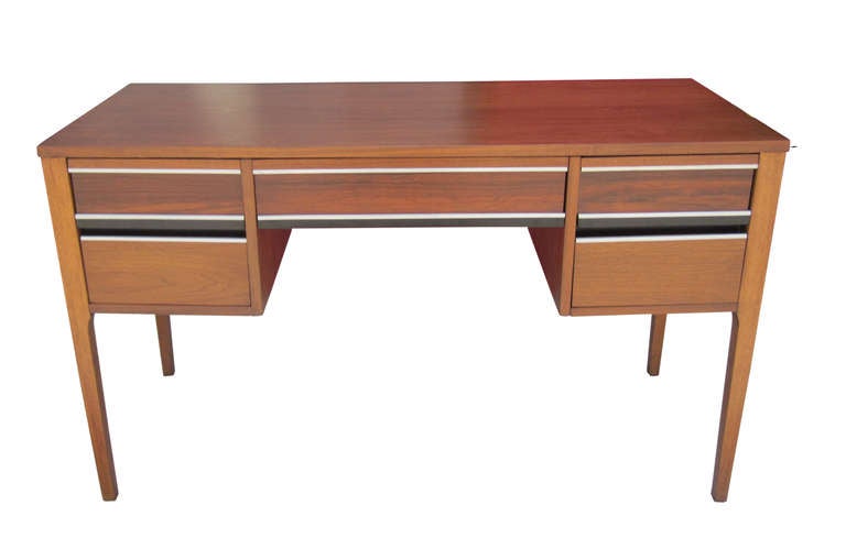 This mid-century modern desk in walnut features five drawers delineated by ebonized wood and chrome inlay. The compact foot-print of the piece makes it ideal for a range of settings.