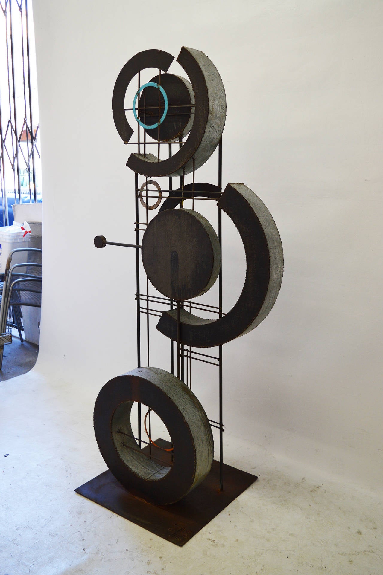 Brutalist metal sculpture with circle theme repeated with various sizes supported by vertical and horizontal steel rods and highlighted with colorful inserts.