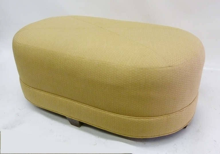 This 1960s ottoman features a large oval surface beautifully upholstered in yellow jacquard arranged in a diamond pattern. The piece rests on four dark wood feet.