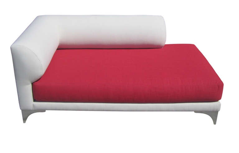 This stylish yet playful chaise lounge from the 1980s features an upholstered frame in cream fabric set off by a cadmium red seat cushion. The chaise rests on stylized bracket feet in cast aluminum/