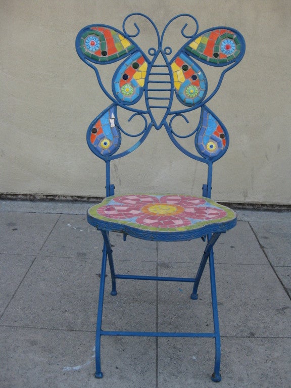 This pair of whimsical, outdoor chairs, one blue, one green, feature seat backs that depict a butterfly and dragonfly respectively. The frames of the chairs are heavy weight metal and are inset with colorful ceramic mosaic.