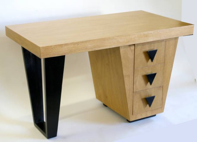 This bleached mahogany desk by Paul Laszlo features three drawers each with  a triangular black stained wood knob. Above the drawers is a pull out extension for extra work space. The row of drawers is counterbalanced by a three sided black stained