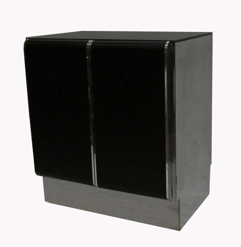 This modern pair of chrome nightstands feature black leather doors that open to reveal a small pull-out drawer and a shelf.