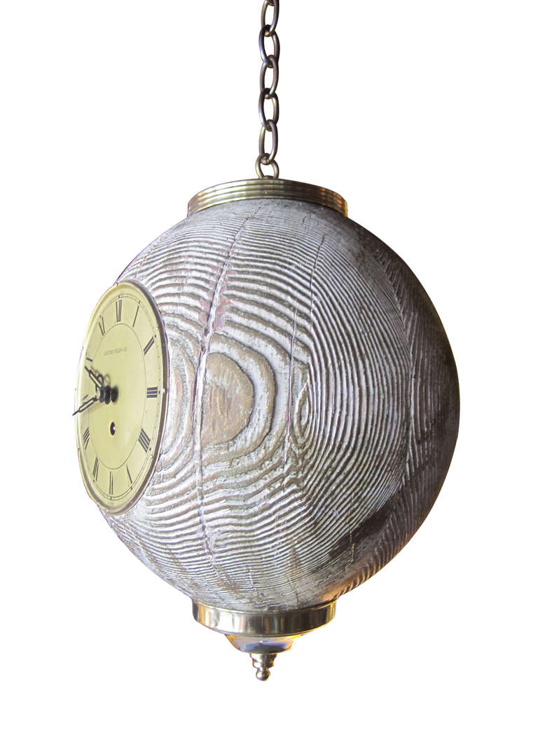 This spherical wooden pendant features a brass clock face with roman numerals and two working hands. The cerused wooden sphere, which is decorated with a ribbed brass canopy and base, is lightly painted with a golden sheen. Clock face reads 