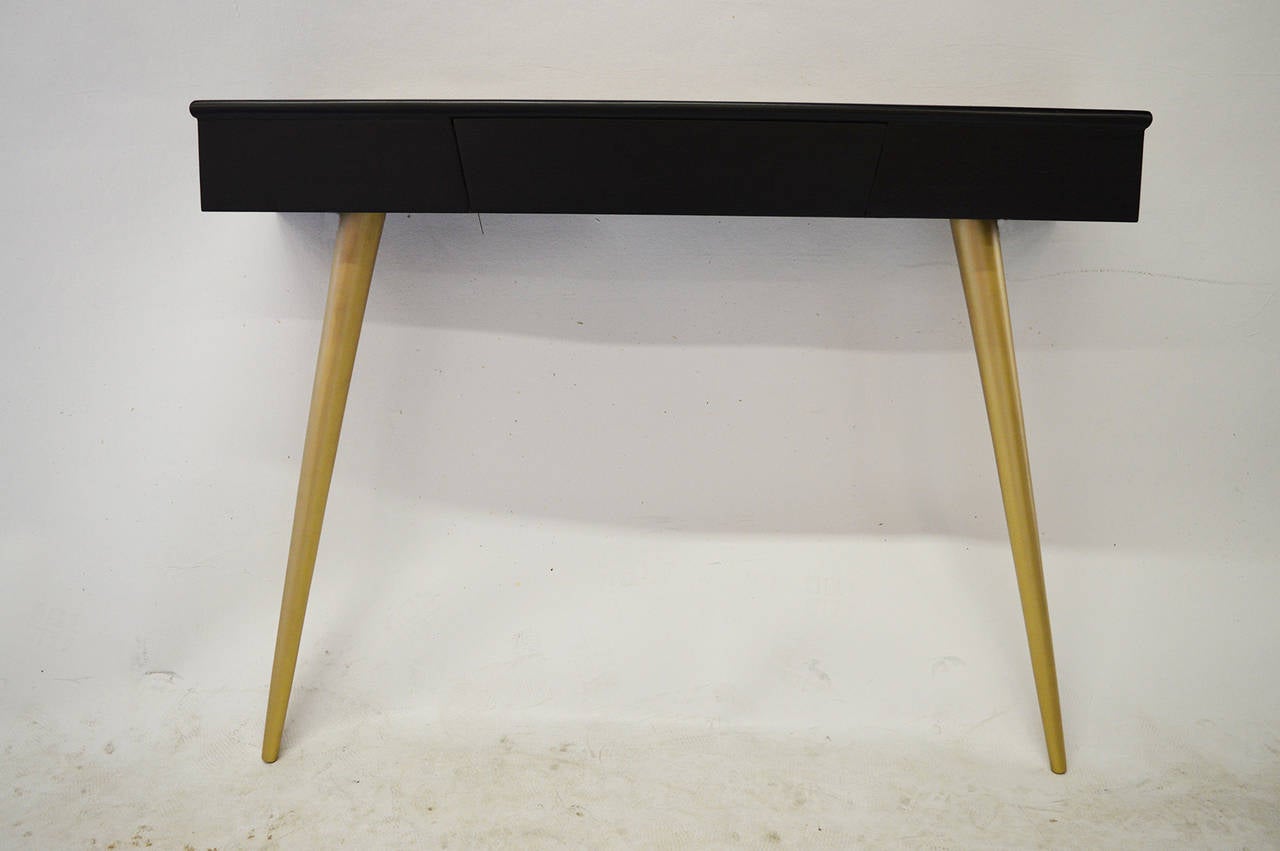 This chic wall hanging console is made of ebonized walnut. 
It features 2 front gilded tapered legs and a drawer.