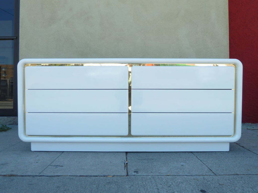 This glamorous 1970s dresser by Glenn of California features gently curved edges and a rich white lacquer finish. The six drawers are set off by a band of inset brass. Each drawer opens with a hidden indentation on the outermost side. The dresser