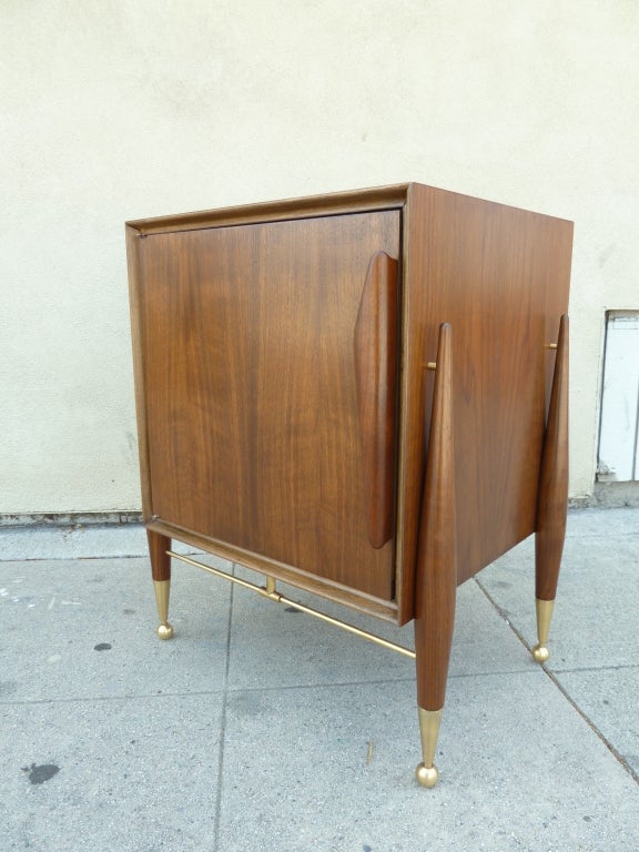 This Italian mid-century modern side table with enclosed cabinet, features four tapered legs which adhere to the outside of the unit using brass connectors. The base of each leg is finished in a tapering brass cap that ends with an elegant