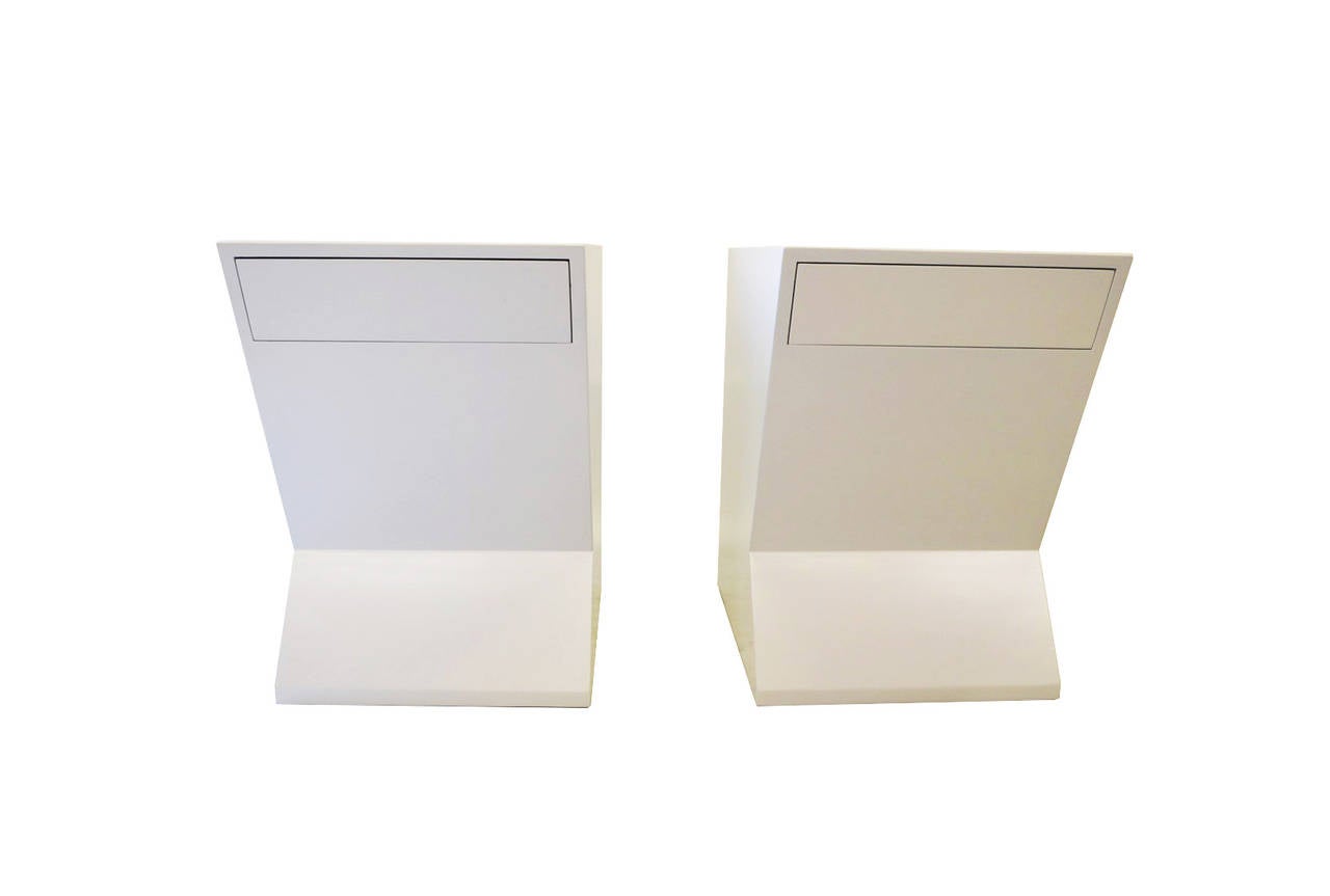 This pair of sculptural nightstands or side tables feature an unique angular form and seamlessly integrated push-to-open drawer. The tables are newly refinished in white lacquer balancing their playful form with modern sophistication.