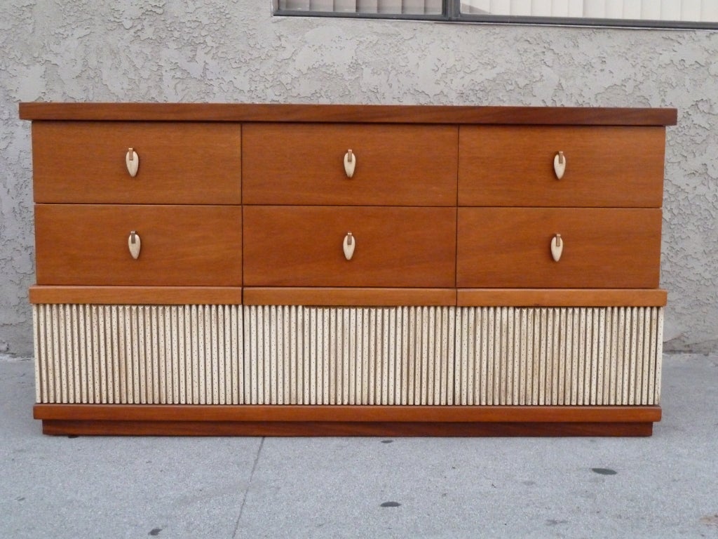 This rare mid-century dresser by American of Martinsville offers plentiful storage with nine drawers. The blond mahogany body is embellished with a reeded section near the bottom, which function as the third row of drawers. The top six drawers are