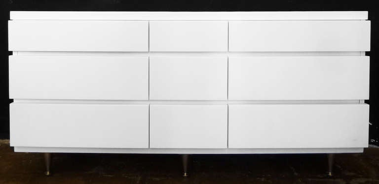 This elegant, mid-century modern dresser by Bassett features nine drawers finished in rich white lacquer. The chest of drawers rests on six tapered legs capped with brass feet.