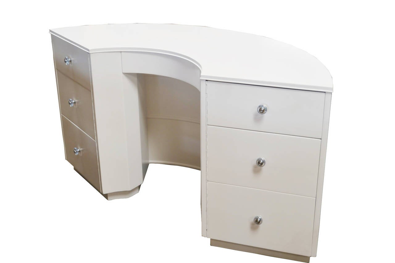 This curved half circle desk features six swing-out drawers that flank a single central pen drawer. The back of the desk has two open shelves for storage or display. This piece, recently refinished in white, has  Lucite knobs. We have the same desk