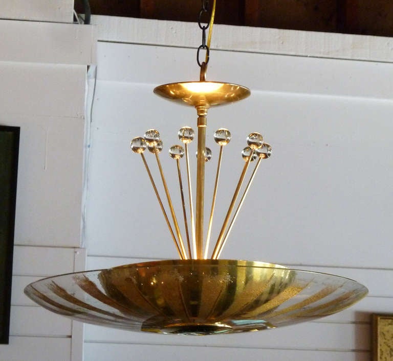 This sophisticated mid-century design from Lightolier features a curved clear glass bowl with gold radiating accents inset with a smaller brass diffuser. Surmounting this are numerous brass and glass “rays,” which extend upwards towards the original