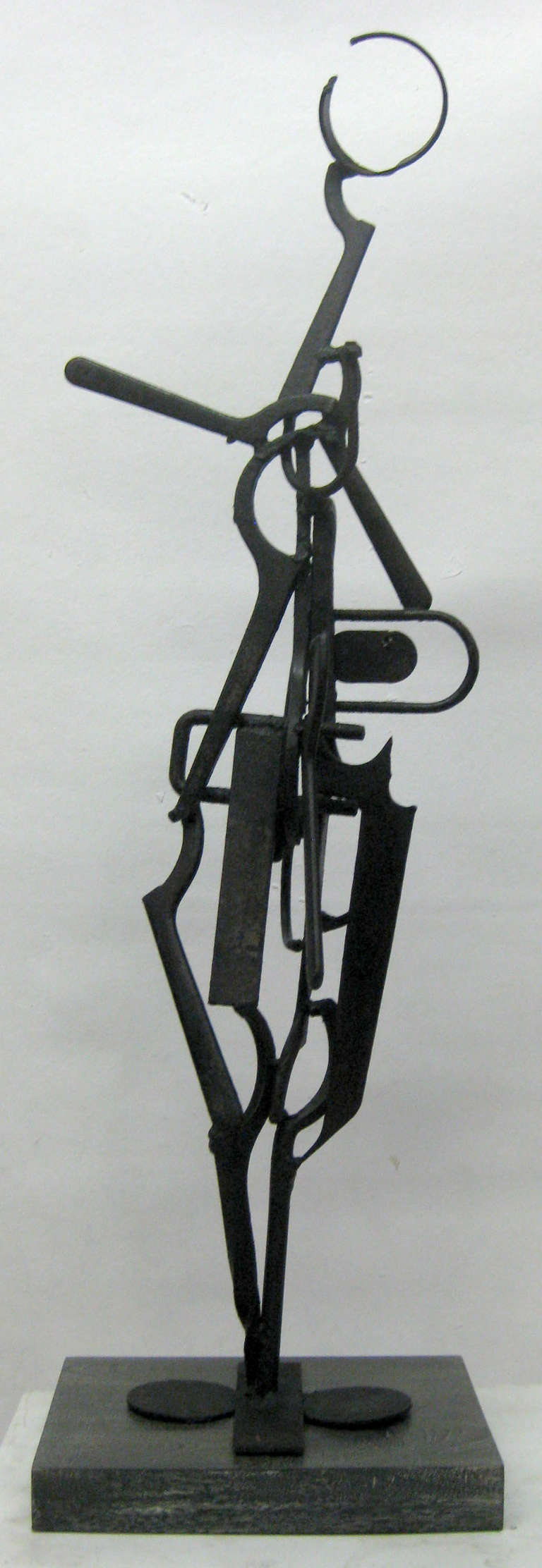 This Brutalist sculpture made of iron, is comprised of various tool parts arranged in a figural form and then painted black. The slightly humanoid piece sits atop a cerused wood base.