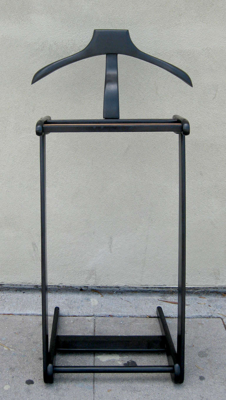 A minimal valet featuring a coat hanger, shoe rack, and storage shelf rendered almost entirely in ebonized wood. The hanging rod features a flat, ribbed top surface in lighter wood.