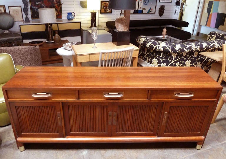 This functional mid-century modern credenza features three drawers and four doors which provide plenty of  storage. The walnut case piece is accented with ribbed door fronts,solid  copper drawer and door pulls and brass feet. The inside left drawer