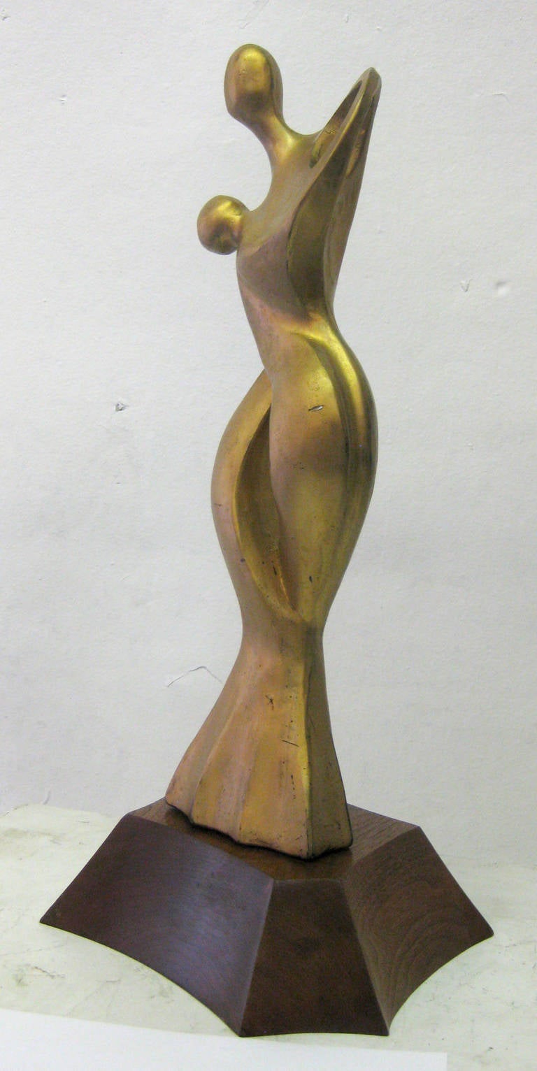 An gilded sculpture of an entwined couple rendered in an abstract, almost surreal fashion. The sculpture sits upon a wooden base in an abstract form that is not attached, as shown.