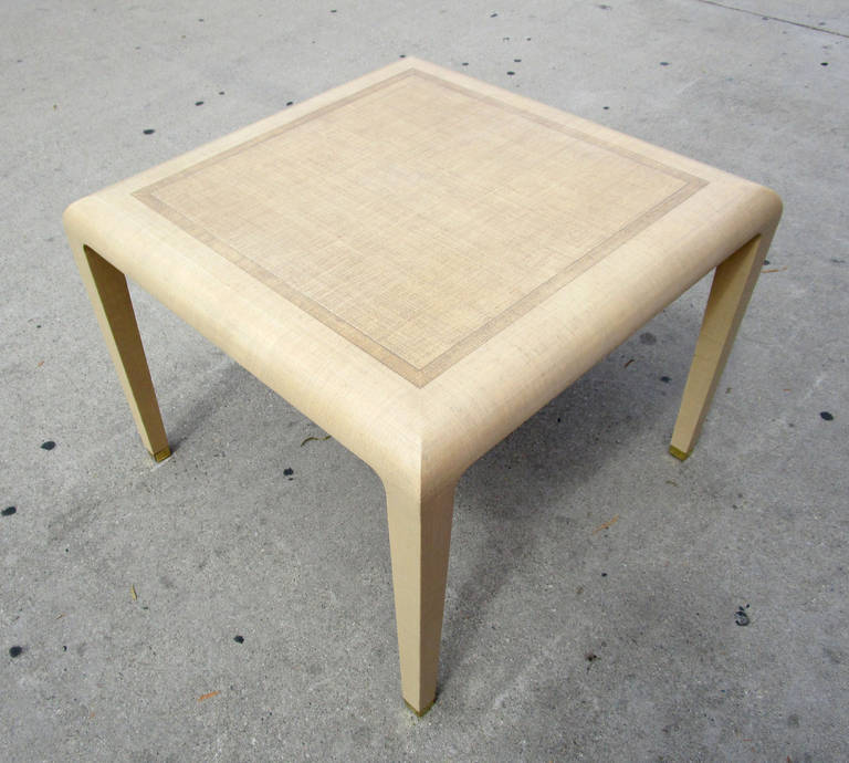 This square table features a raffia frame with an elegant shape and a three-tone square pattern on top. The slightly tapered legs ending in brass sabots lend this piece a subtle glamour. The lines and material of this piece reference the designs of