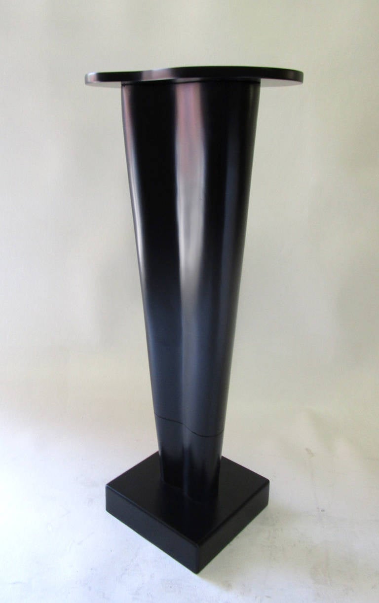 This pedestal features a square base that supports a tapered free form-shaped column which is topped off by a similarly shaped surface. The entire piece has recently been refinished in black lacquer, subduing the playful form of this piece. 
Base