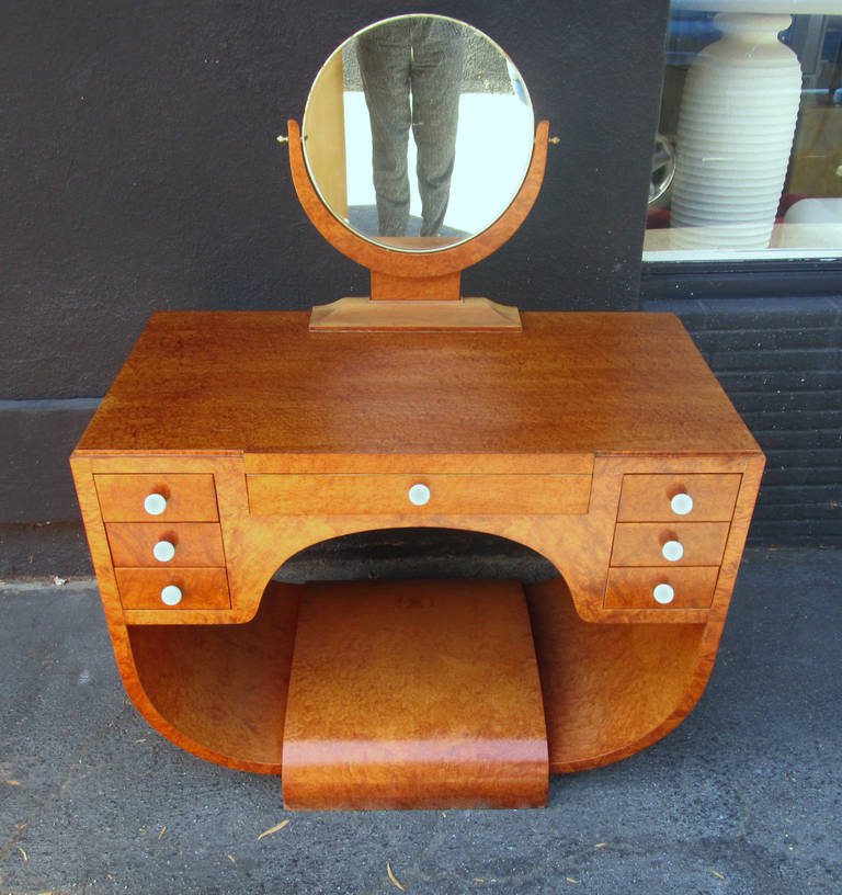 This art deco vanity features an elegant, curved frame in gorgeous bird's-eye maple topped off by a circular swiveling mirror. The seven drawers have white ceramic knobs with a black craquelure. This piece strongly resembles the model AR1537 / NR