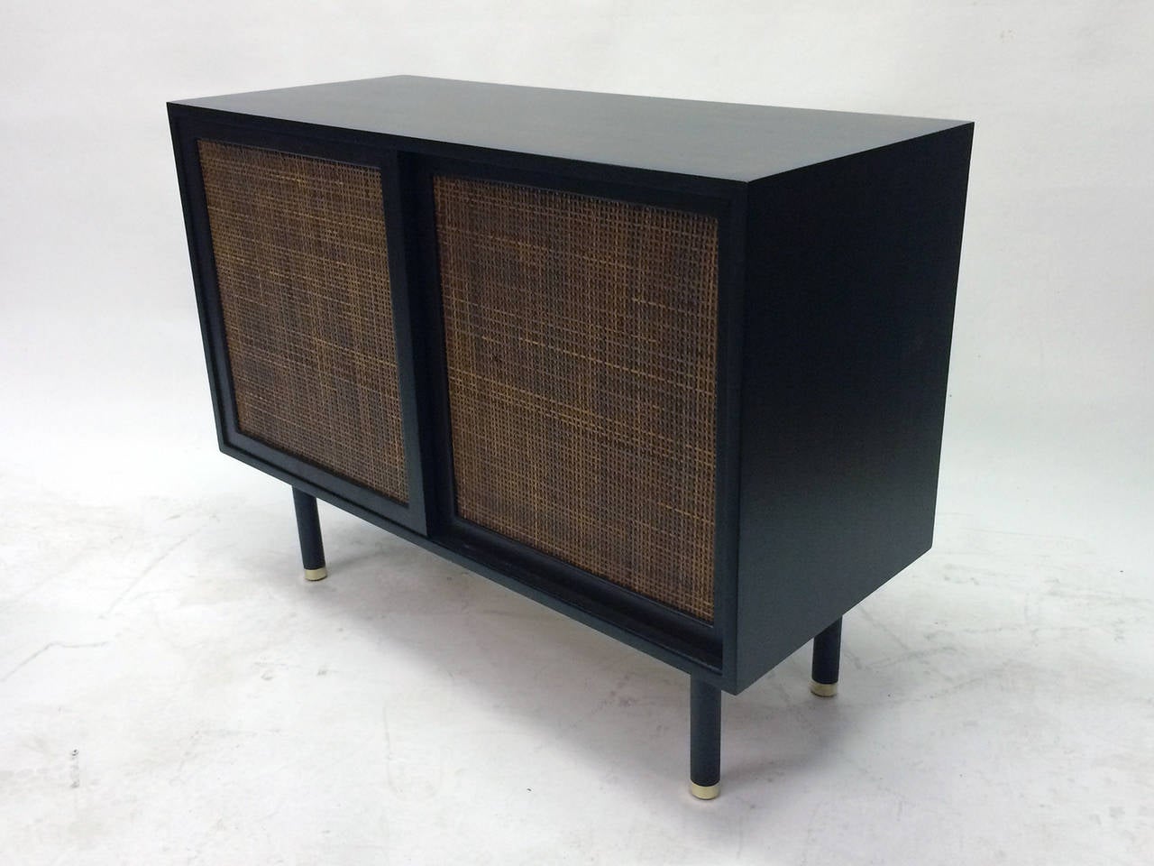This buffet features two sliding doors opening on one  shelf on one side and 3 drawers on the left.  Doors are fronted with rattan. Beautiful dark grain pattern in the wood.  Brass caps on round legs.
The piece retains the labe 