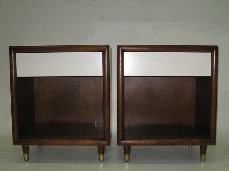 This pair of mid-century modern nightstands by Furniture Guild of California feature walnut casings housing a single drawer finished in off-white lacquer; below is an open storage space for books or objects. The nightstands are supported by four