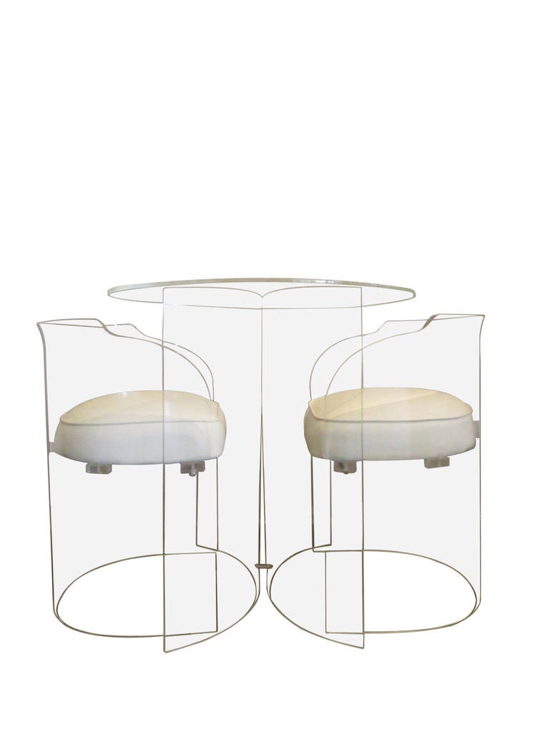 A distinctly 1970s Lucite set of two chairs and a smaller-sized table perfect for playing games or as a dining table for two. The chairs are comprised of a Lucite barrel with a single white vinyl floating seat attached. The base of the table is two