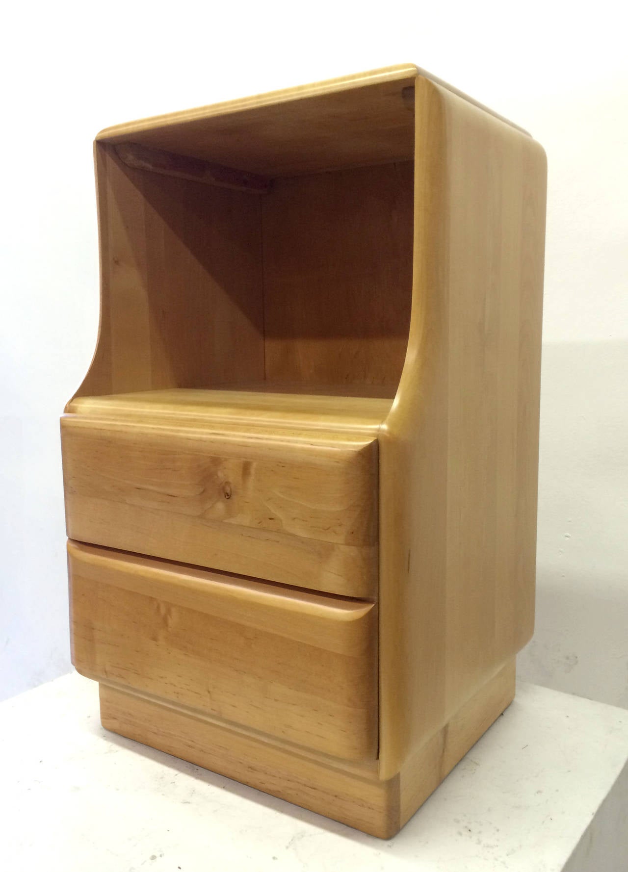 This pair of blonde wood nightstands feature a large storage cavity that sits upon a single drawer disguised as two. The slightly curved edges coupled with the blonde solid maple and excellent craftsmanship strongly recall the designs of Heywood