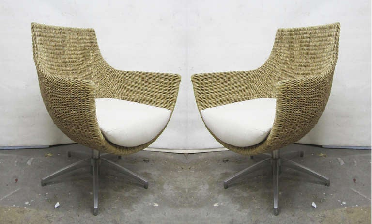 The frames of this pair of egg-shaped armchairs are rendered in wicker and completed by a small white linen cushion. The chairs rest upon a five-pointed cast aluminum base.