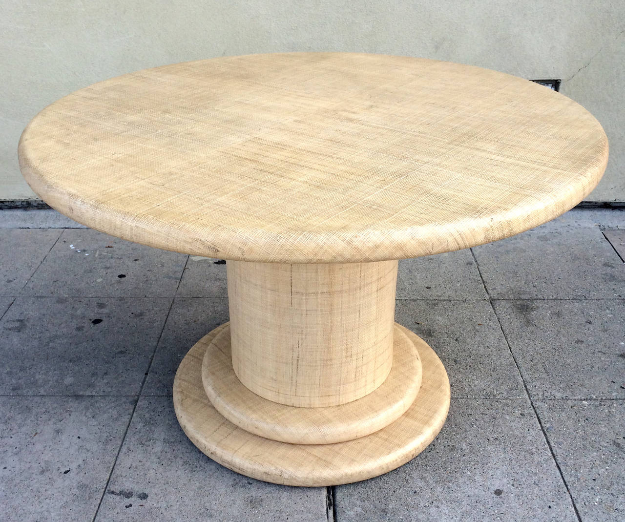 This chic, circular dining table by Harrison Van Horn is entirely wrapped in grasscloth with a clear protective coating. The base, comprised of two circles of wrapped wood, supports a round column that holds up the 4 foot wide surface.  Underneath