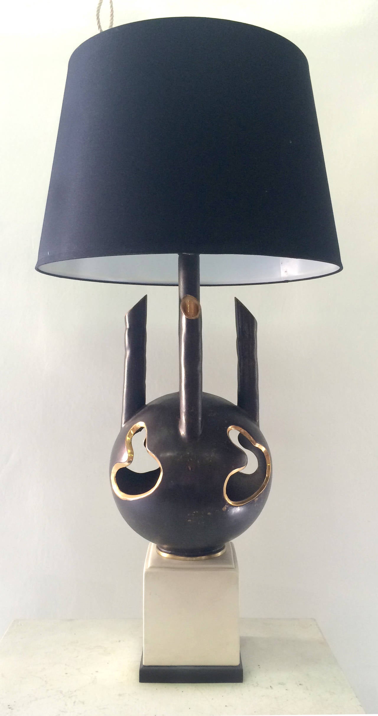 This unusual ceramic table lamp has an arresting, strong design that is emphasized by the size of this piece. The ceramic base features spherical body with gold-rimmed cutouts and four tall, slender hollow branches. It sits upon a white rectangular